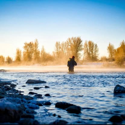 Angler wading a misty Wyoming river at sunrise