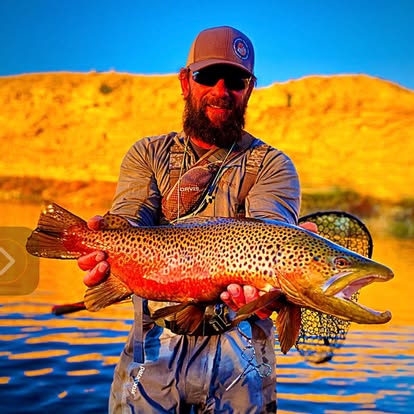 Angler with a large rainbow trout, golden canyon backdrop