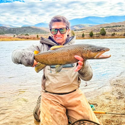 Client with a huge brown trout, Wyoming mountains behind