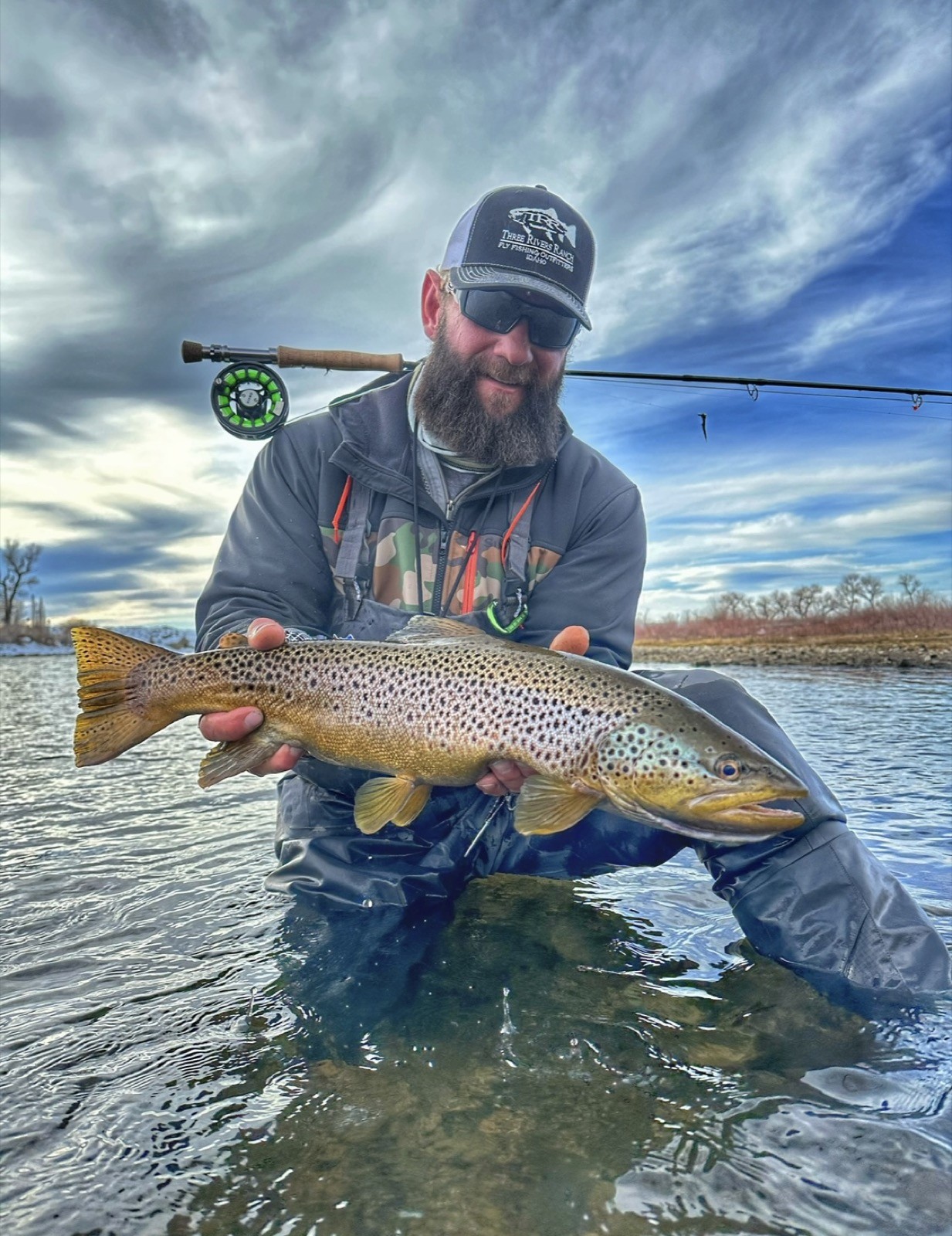 Angler with a trophy brown trout under a dramatic Wyoming sky